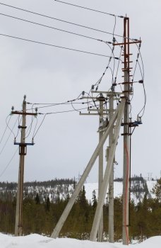 Electric line on concrete piers with reclosers on the background of snow-covered forest