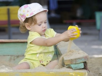 Little girl playing in the sandbox. Today the sand of the cups.