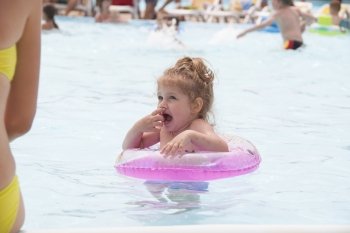  Two-year-old girl bathes in a public pool. Girl again entered the water and frozen from the cold water. Summer day.