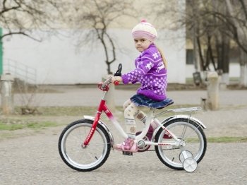 A four year old girl goes on a Bicycle on an asphalt-paved road. A warm spring day.