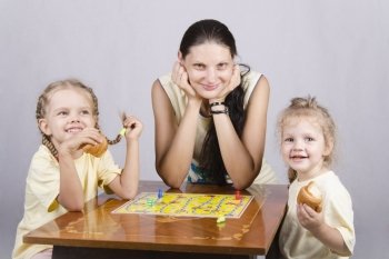 A mother and two daughters are sitting at the table and play a Board game