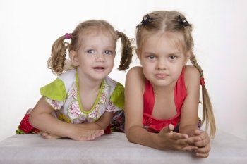 Two girls lie on your stomach, leaning on his hands and looking in the frame. Studio light background