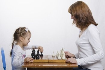 Mom and daughter playing at a table in chess. Mother teaches daughter game