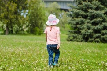 Little girl walking on the grass with dandelions