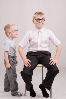 Twelve year old boy with glasses sitting on a chair, standing next to a year-old boy