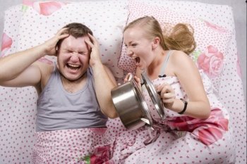 A couple lying in bed. Girl brutally awakened a sleeping guy, slamming the lid on the pan. Photo on top