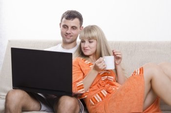 A boy and a girl sitting on the couch. A guy sitting with a laptop, a girl clung to him a Cup of tea.
