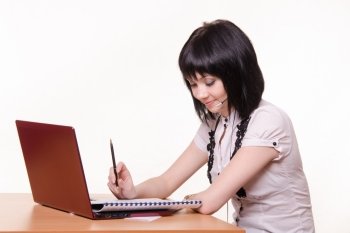 Cute little girl sitting at a table in the call center with laptop in white blouse. Girl - call-center employee at the desk with documents