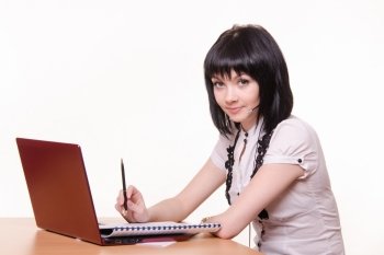 Cute little girl sitting at a table in the call center with laptop in white blouse. Girl - call-center employee at the desk