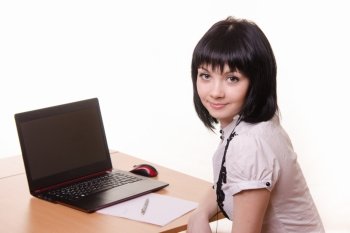 Cute office girl sitting at a table with a laptop in white blouse. The girl at the table with a laptop