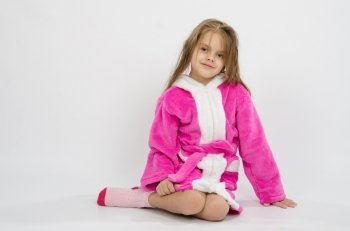 Six year old girl with wet hair in a bathrobe on a light background. Six year old girl in a bathrobe