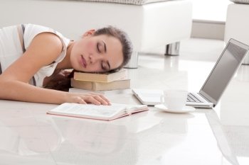 The Young Beautiful Woman Sleeping on the Floor with the Laptop, Textbooks and a ?up of ?offee on the Pile of Books In The Apartmen