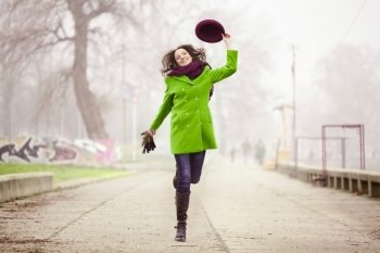 Happy Young Woman Jumping with a Hat at the Footpath in the Foggy  Day