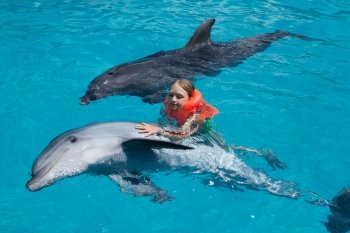 Little Girl Swimming with two Dolphins in Swimming Pool