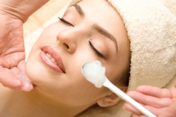 Health spa: close-up of a beautiful relaxing woman having facial massage with cream