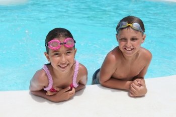 Happy children, girl and boy, relaxing on the side of a swimming pool wearing pink and grey goggles