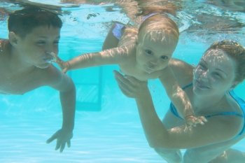 Underwater family in swimming pool. Mother teaching her kids 