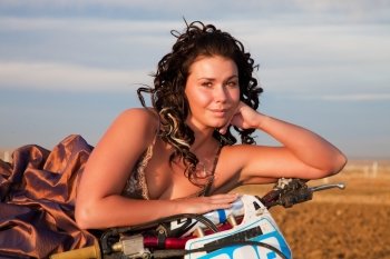 A young girl in her prom dress laying on her motocross bike in a trash the dress shoot.