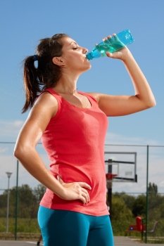 Young woman drinking mineral water on a basketball court