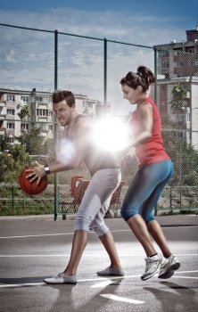 Young man and woman playing basketball on the playground