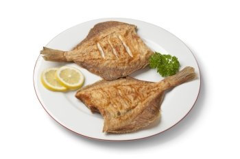 Dish with fried plaice, lemon and parsley on white background