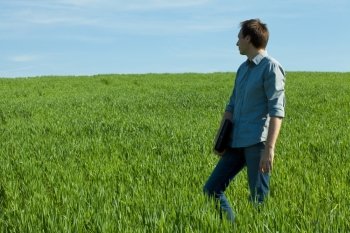 young man standing with a laptop in the green field 