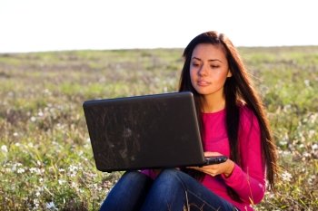 young beautiful woman with a laptop sitting in the field on sky background 
