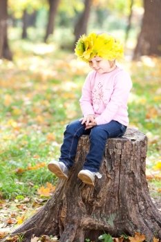 beautiful little girl in a wreath of maple leaves sitting on stump