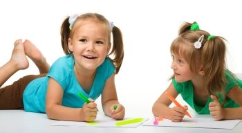 Two little girls draw with markers while laying on floor, isolated over white