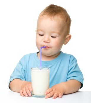 Cute little boy is drinking milk using straw while sitting at table, isolated over white