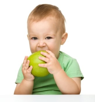 Cute little child is eating green apple while sitting at table, isolated over white