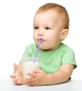 Cute little boy is drinking milk using straw while sitting at table, isolated over white