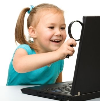 Cute little girl is looking at her black laptop through magnifier, isolated over white