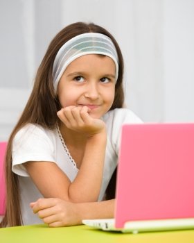 Cute little girl is sitting at table with her pink laptop