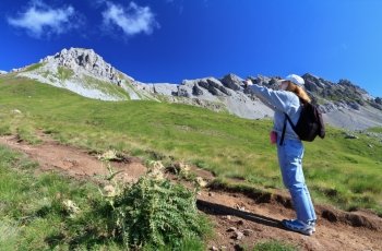 female hiker on a footpath is photographing alpine landscape 