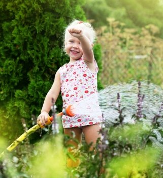 Little girl watering the grass in the garden