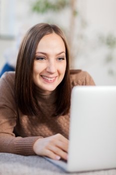 photo of smiling caucasian woman lying on the couch and chatting with computer
