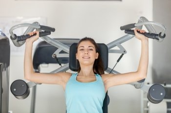 Photo of smiling caucasian brunette training her upper body in gym