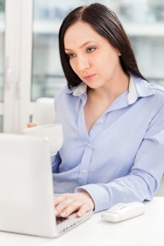Photo of aucasian businesswoman working with notebook while drinking coffee in the office