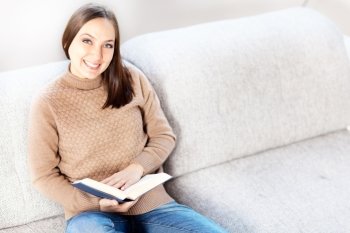 Photo of casual smiling woman sitting on the sofa with a book