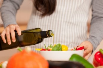 Closeup of woman pouring olive oil into the colorful salad