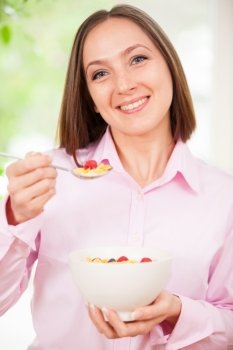 Portrait of smiling brunette woman holding a bowl with corn flakes with berries in her hands