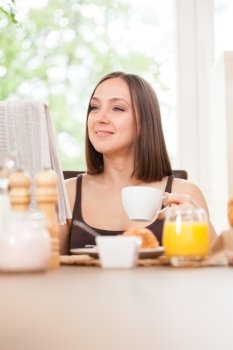 Photo of caucasian brunete woman reading a newspaper while having breakfast at home