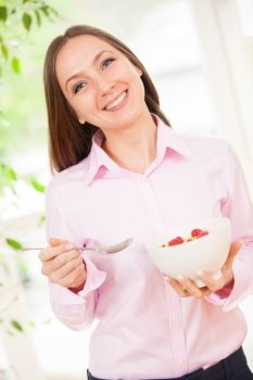 Smiling woman holding a bowl with corn flakes with berries in her hands