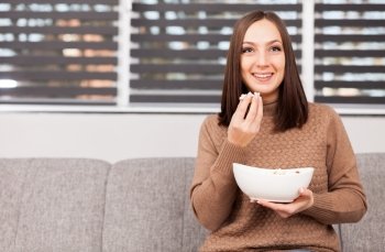 Photo of brunette caucasian woman eating popcorn while looking tv at home