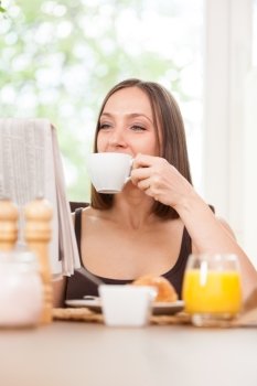 Photo of caucasian brunete woman reading a newspaper while having breakfast at home