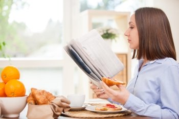 Photo of brunette businesswoman reading the newspaper while having breakfast at home