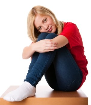 Cute teenager girl feeling lonely sitting alone with knees pulled up and arms around legs, isolated.