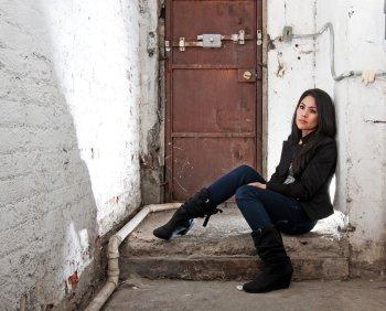 Beautiful Caucasian girl sitting on concrete floor in basement in front of brown door