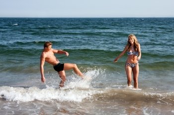 Beautiful young couple playing in the ocean splashing water, heaving fun on a summer day